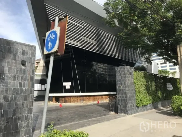 Retail Space for rent in Sathon, Bangkok - Side view of the angular façade with metal louvres and trimmed hedges along the boundary wall.