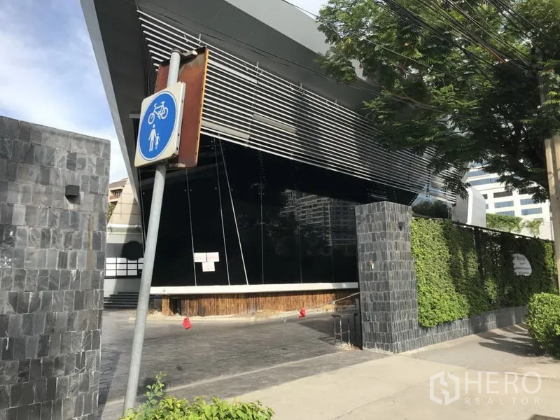 Retail Space for rent in Sathon, Bangkok - Side view of the angular façade with metal louvres and trimmed hedges along the boundary wall.