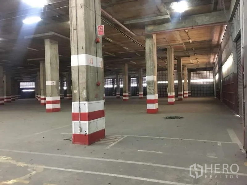 คลังสินค้า ให้เช่าในPhra Pradaeng, Samut Prakan - มุมภายในโกดังพร้อมประตูม้วน ป้ายความปลอดภัย และไฟส่องสว่าง