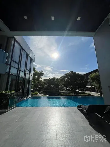Townhouse for rent in Saphan Sung, Bangkok - Resort-style swimming pool beside a contemporary clubhouse under sunny skies.