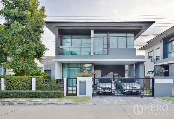 Detached House for rent or sale in Bang Kapi, Bangkok - Modern two-storey detached house with gated frontage, two-car covered carport and large glass balcony in a landscaped estate.
