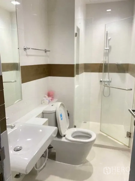 Condominium for rent in Phra Khanong, Bangkok - Modern white bathroom with glass-enclosed shower, sink and toilet.
