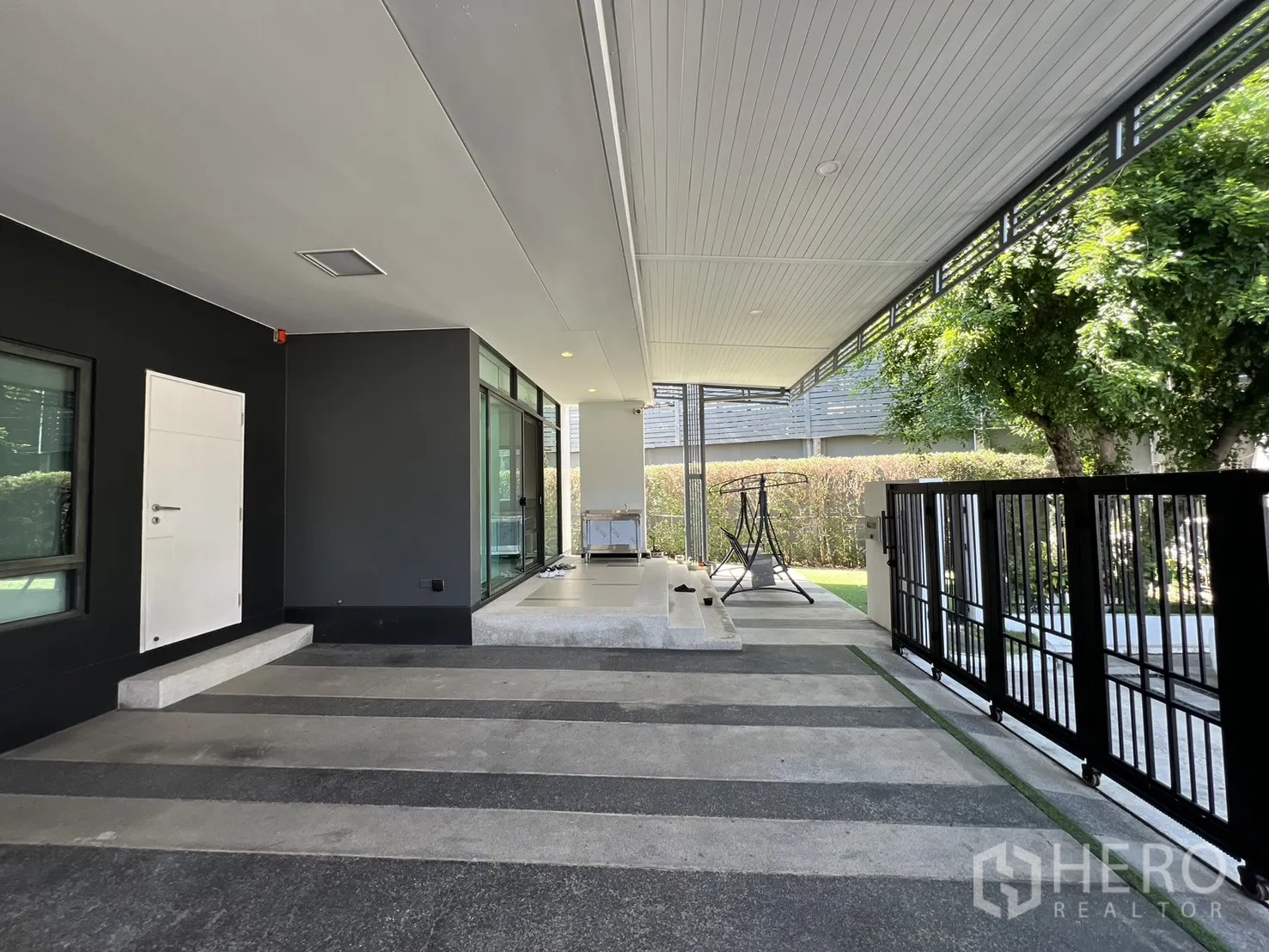 Detached House for sale in Bang Kapi, Bangkok - Carport beside floor-to-ceiling windows and black metal gate to the garden.