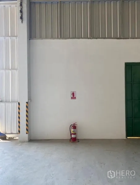 货栈 出租在Mueang Rayong, Rayong - 金属滑门旁白色墙面上的灭火器，安全设施。