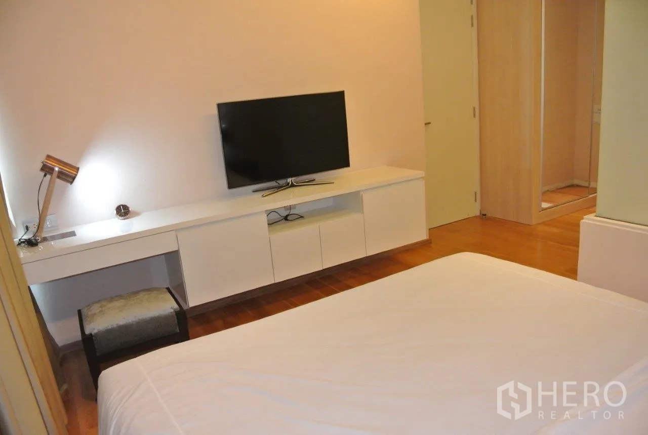 Condominium for rent in Watthana, Bangkok - Primary bedroom media wall with long built-in desk, TV unit and mirrored wardrobe.