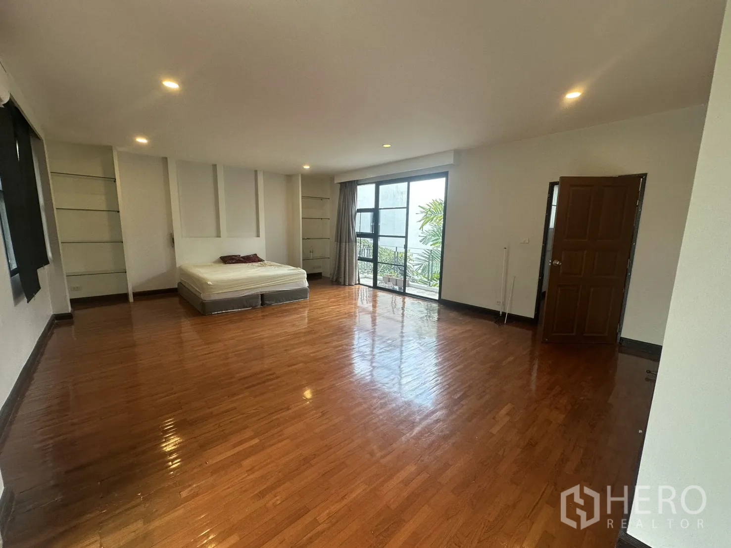 Detached House for rent in Watthana, Bangkok - Bedroom with balcony door, wood floors, and recessed lighting.