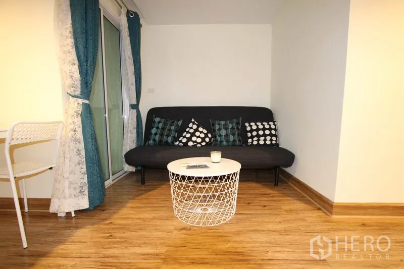 Condominium for rent or sale in Wang Thonglang, Bangkok - Cozy lounge corner with sofa, round wire coffee table, and sliding door to the balcony.