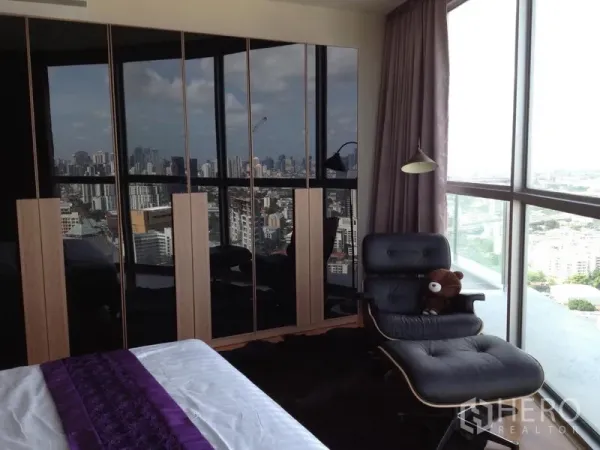 公寓 出租在Watthana, Bangkok - 卧室转角配落地窗，全景城市天际线，亮面衣柜与躺椅。