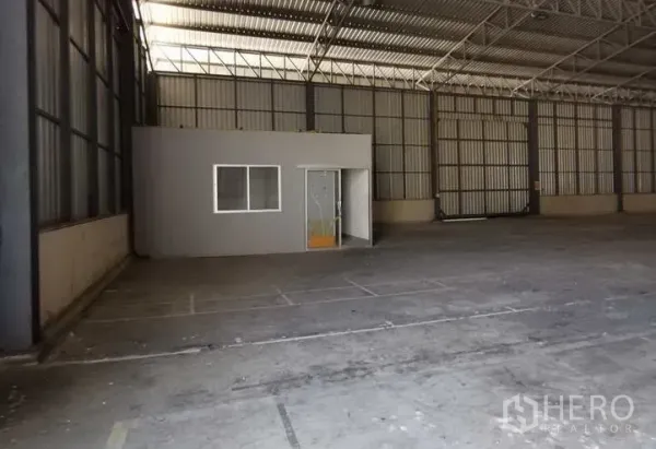 Warehouse for rent in Mueang Samut Prakan, Samut Prakan - Open storage hall featuring a built‑in compact office room and metal wall panels.
