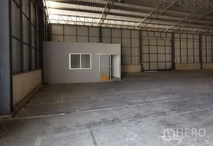Warehouse for rent in Mueang Samut Prakan, Samut Prakan - Open storage hall featuring a built‑in compact office room and metal wall panels.