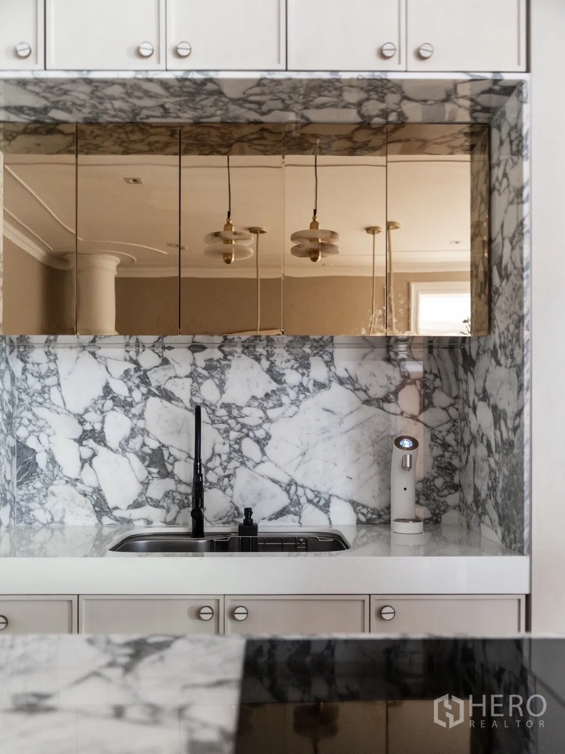 Detached House for rent or sale in Phra Khanong, Bangkok - Close-up of marble kitchen backsplash, mirrored cabinets and sink with black faucet.