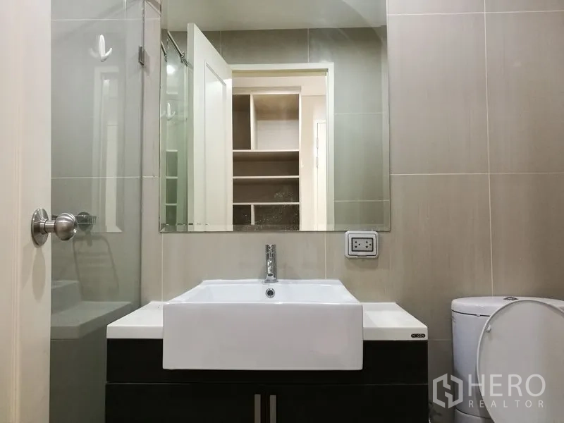 Condominium for rent in Ratchathewi, Bangkok - Modern bathroom featuring a square vanity basin, large mirror, glass shower and toilet.