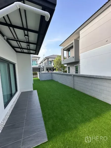 独立式住宅 出租在Bang Phli, Samut Prakan - 侧院人工草坪与瓷砖露台，围墙和屋檐。