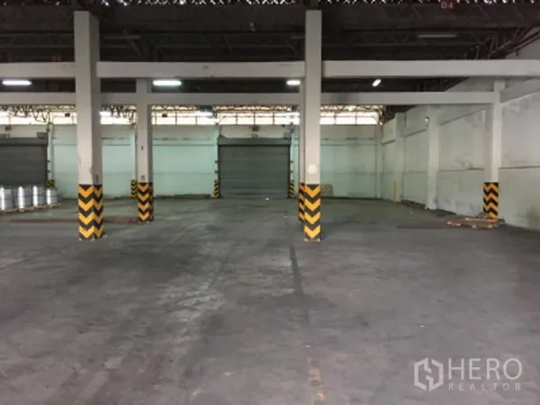 货栈 出租在Pathum Thani - 面向多扇卷帘门的仓库内部视角，连接装卸区与空旷作业面。