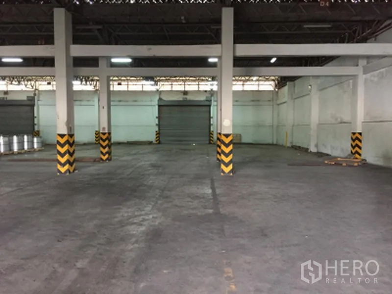 货栈 出租在Pathum Thani - 面向多扇卷帘门的仓库内部视角，连接装卸区与空旷作业面。