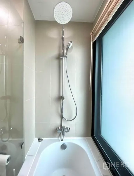 Condominium for rent in Khlong Toei, Bangkok - Bathtub with rain shower beside a frosted window in a tiled bathroom.