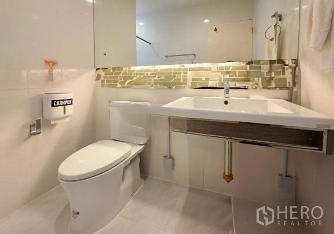 Detached House for sale in Bang Kapi, Bangkok - Second bathroom with long mirror, vanity counter and neutral tile tones.