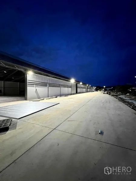 Warehouse for rent in Mueang Samut Prakan, Samut Prakan - Night view of illuminated warehouse row and wide driveway for trucks.