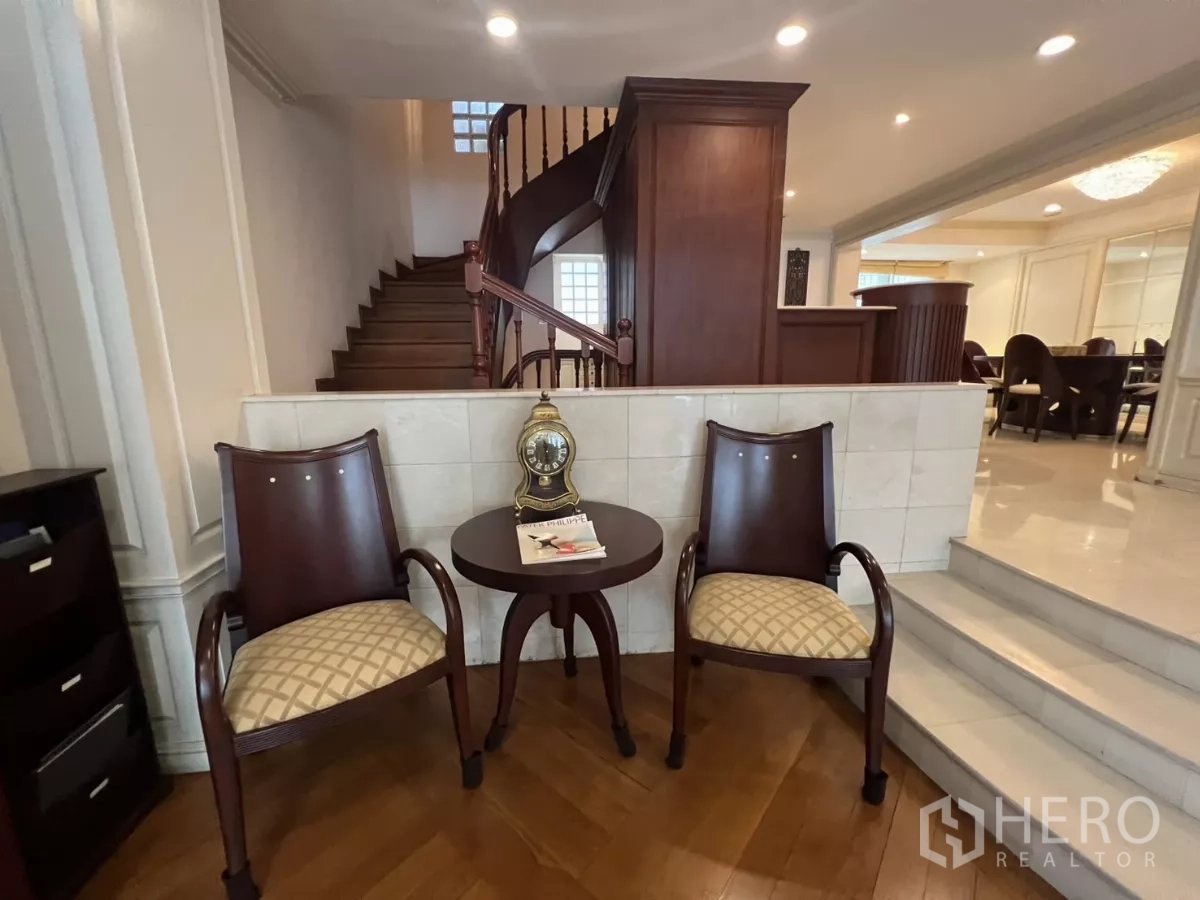 Townhouse for sale in Watthana, Bangkok - Stair hall featuring a wooden staircase, two armchairs and recessed lighting.