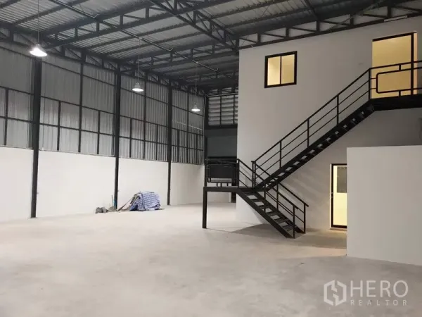 工厂 出租在Lam Luk Ka, Pathum Thani - 仓库内部高挑钢结构屋顶，带夹层办公室与黑色楼梯。