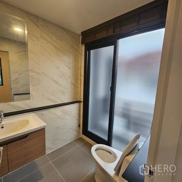 Detached House for rent in Saphan Sung, Bangkok - Bathroom with vanity, toilet and frosted glass door allowing natural light and ventilation.