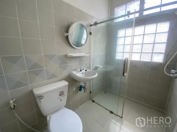 Townhouse for rent in Watthana, Bangkok - Bright bathroom with glass-enclosed shower, toilet and sink beneath a glass-block window.