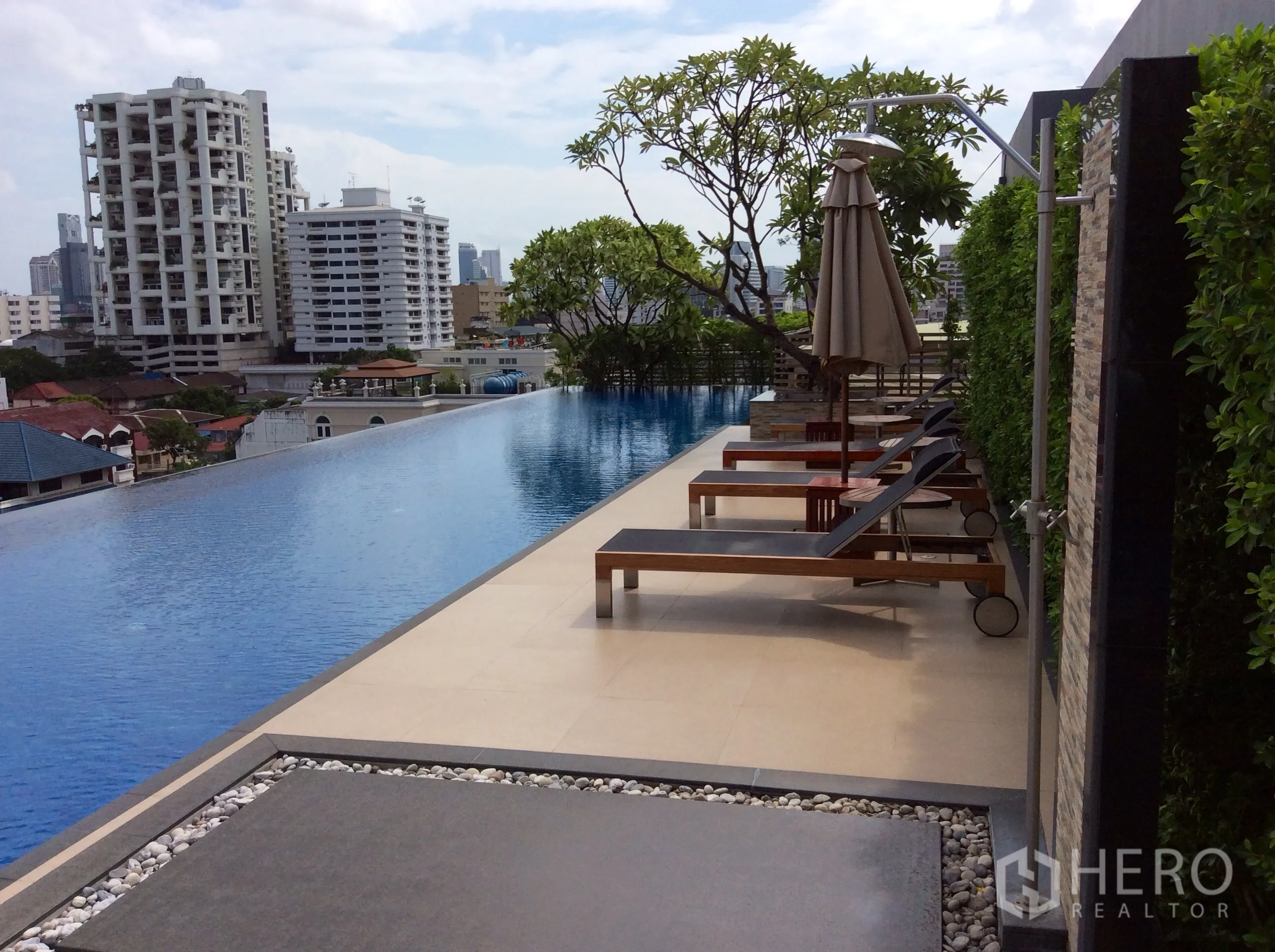 Condominium for rent or sale in Khlong Toei, Bangkok - Rooftop infinity pool with sun loungers and umbrellas overlooking the Bangkok city skyline at a modern condominium.