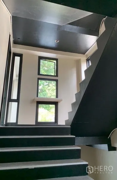 Standalone for rent in Khlong Toei, Bangkok - Contemporary staircase with black steps and tall windows bringing natural light between floors.