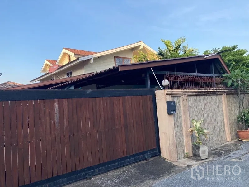 Detached House for sale in Wang Thonglang, Bangkok - Street-side view of the property showing a tall wooden sliding gate and gabled upper floor.