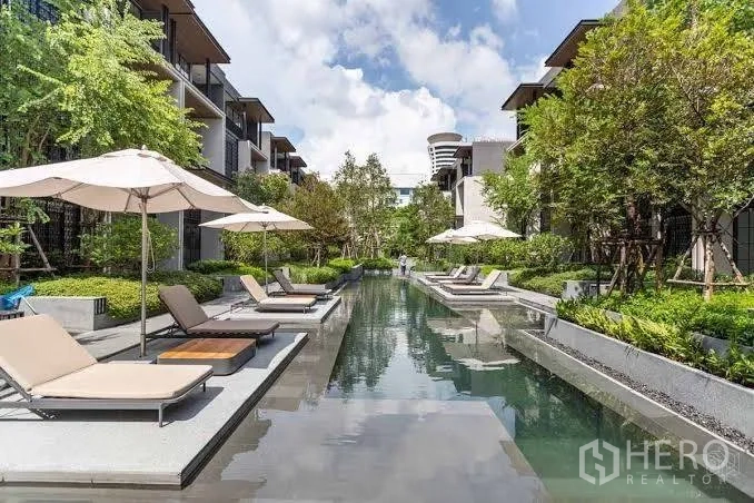 Townhouse for rent in Khlong Toei, Bangkok - Long communal lap pool lined with sun loungers and umbrellas between low‑rise buildings.