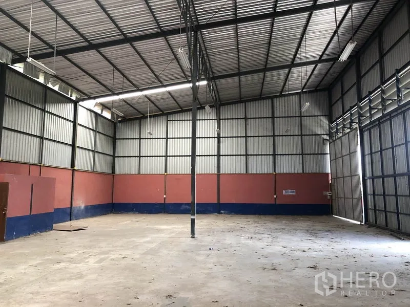 Warehouse for rent in Lam Luk Ka, Pathum Thani - Spacious warehouse with high ceiling, skylight panels, strip lighting and open floor area with sliding access door.