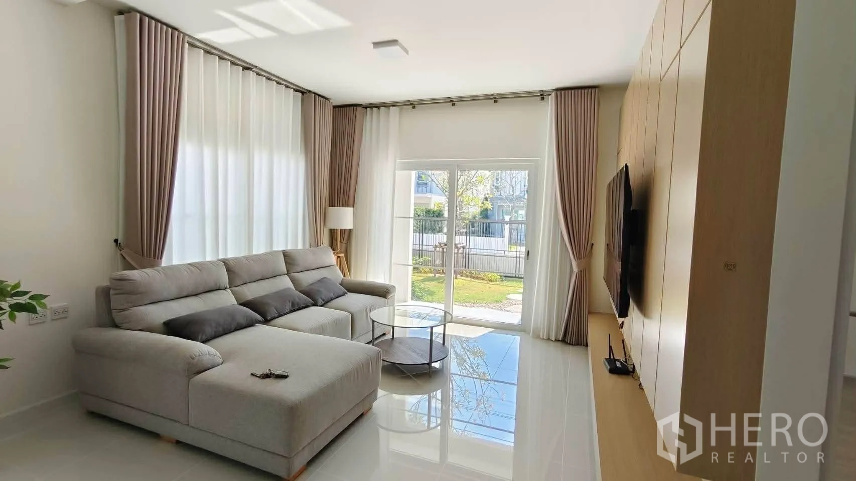 บ้าน for rent in Bang Phli, Samut Prakan - ห้องนั่งเล่นสว่างด้วยโซฟา L โอ่โถง ประตูกระจกสไลด์ออกสวน และผนังบิวท์อินทีวี