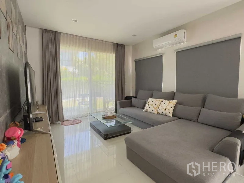 บ้าน ให้เช่าหรือขายในBang Khen, Bangkok - ห้องนั่งเล่นอบอุ่น โซฟาเข้ามุมสีเทา ทีวี หน้าต่างบานใหญ่ และเครื่องปรับอากาศ