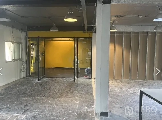 Retail Space for rent in Pathum Wan, Bangkok - Open-plan retail interior with glass double doors and a yellow feature wall under pendant lights in Pathum Wan.