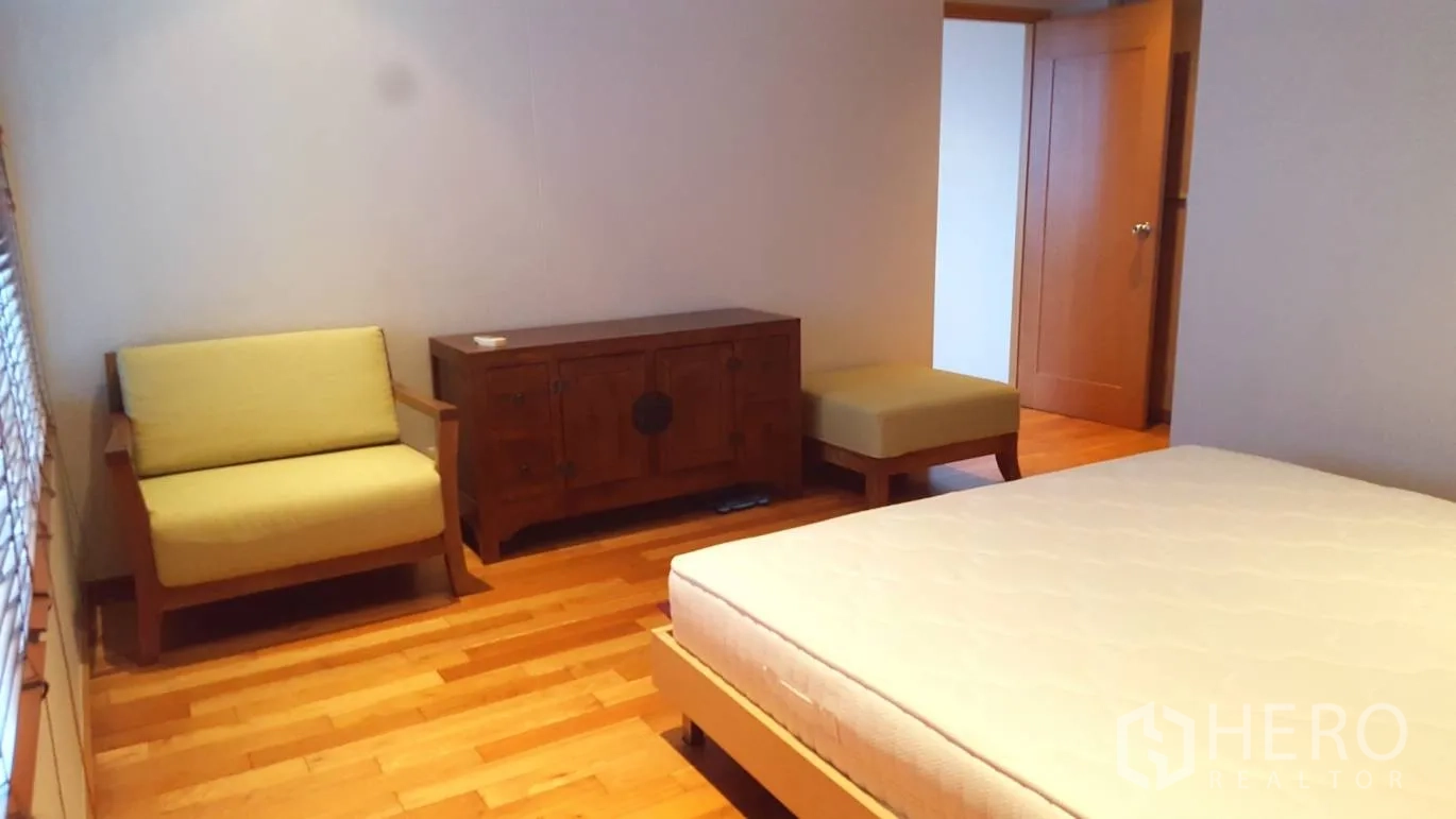 Condominium for rent or sale in Khlong Toei, Bangkok - Warm-toned bedroom with wood floors, a small sofa, wooden cabinet and bed frame.
