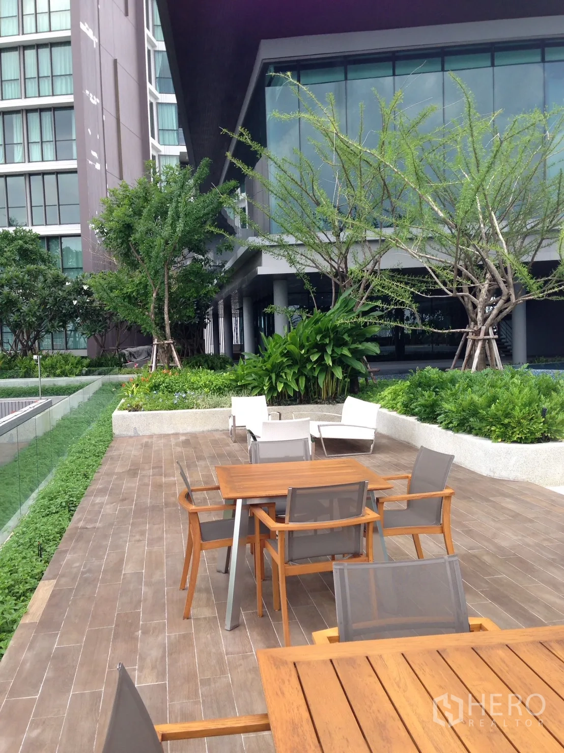 Condominium for rent in Bang Sue, Bangkok - Outdoor terrace with tables and chairs surrounded by landscaped gardens and modern facade.