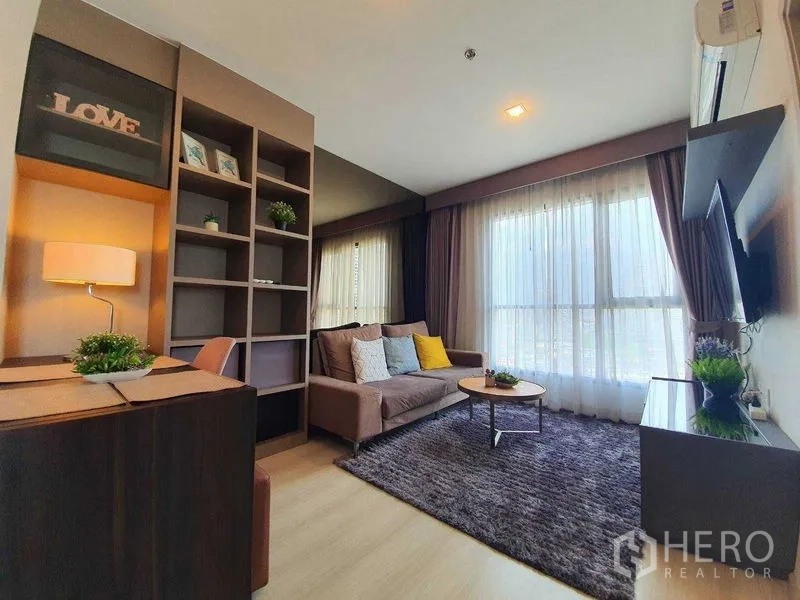 Condominium for sale in Khlong Toei, Bangkok - Open living room with TV wall, coffee table, plush rug, and full‑height windows.