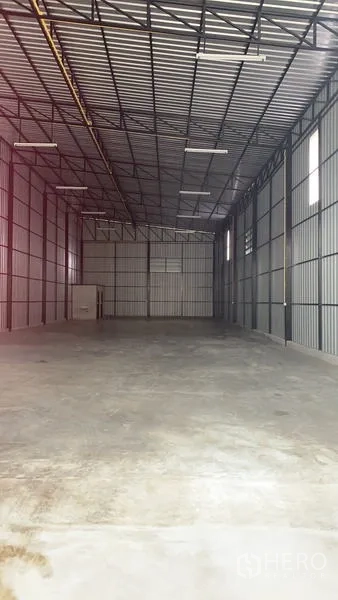 Warehouse for rent in Khan Na Yao, Bangkok - Long-depth view of the high-clearance storage space with ventilation windows and roof trusses.