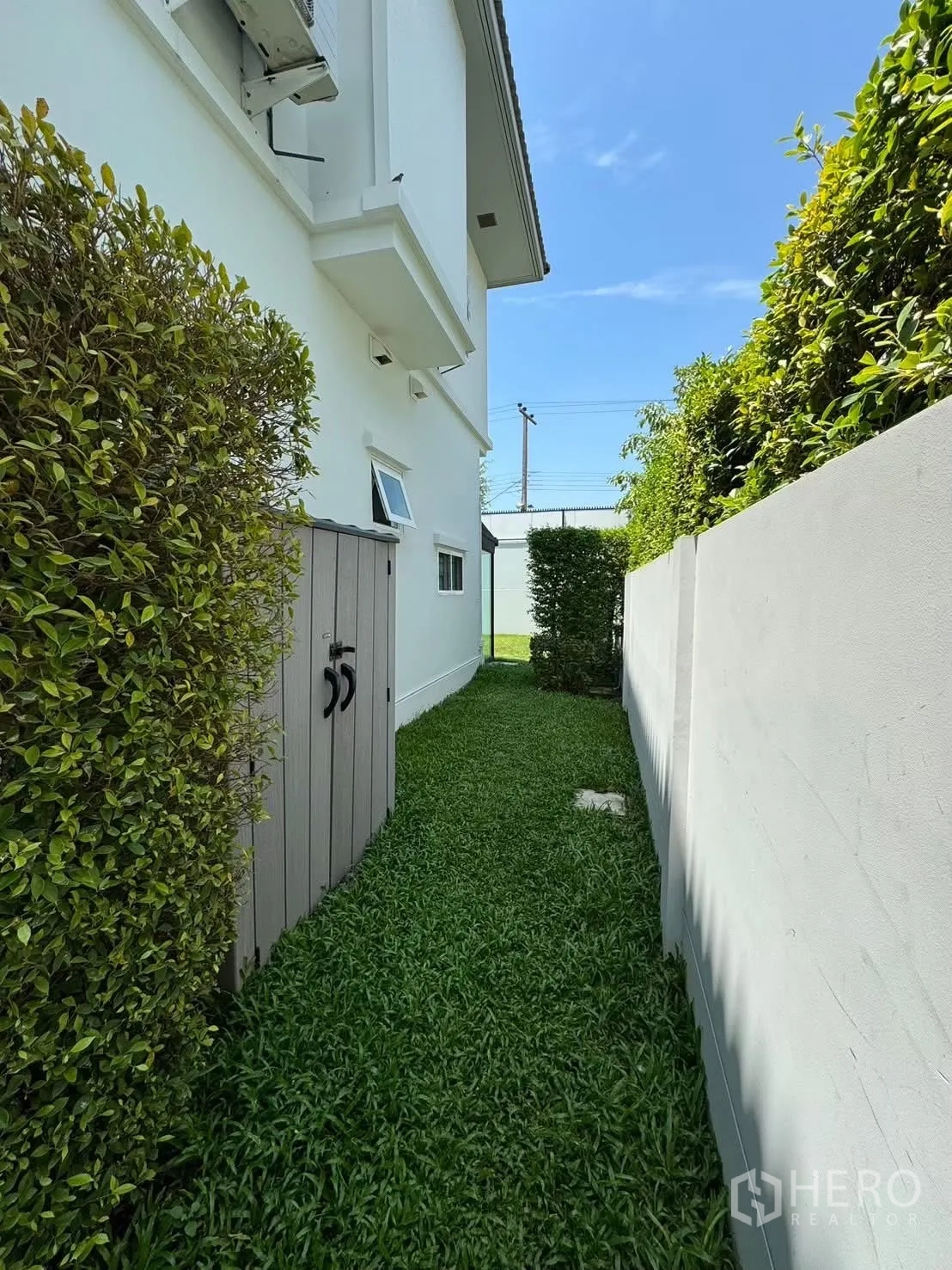 Detached House for rent in Prawet, Bangkok - Side yard walkway bordered by tall hedges and an outdoor storage cabinet.