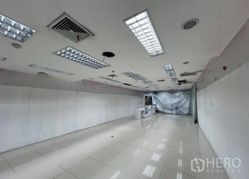 Retail Space for rent - Long retail interior with glossy tile flooring, AC vents and grid lights on the ceiling, vacant and ready for renovation.