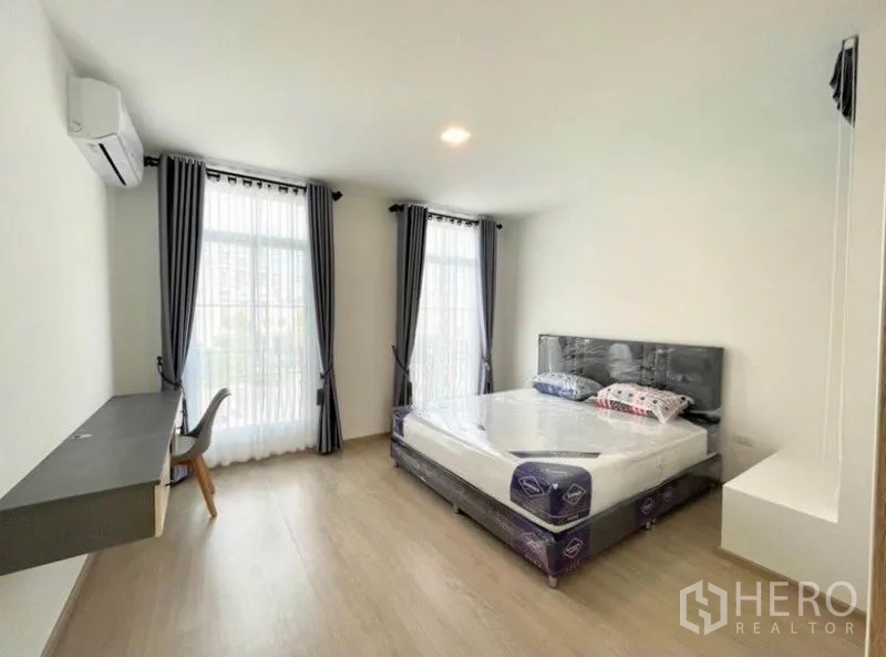 联排别墅 for rent in Prawet, Bangkok - 主卧配大床、书桌、落地窗与深色窗帘。