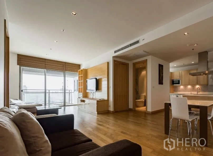 公寓 出租在Watthana, Bangkok - 开放式客厅，木地板与电视墙，旁接厨房和餐区，阳台可观城市景。