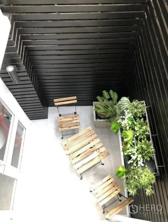Townhouse for rent in Khlong Toei, Bangkok - Compact patio with wooden bistro set and a vertical garden against black slat walls.