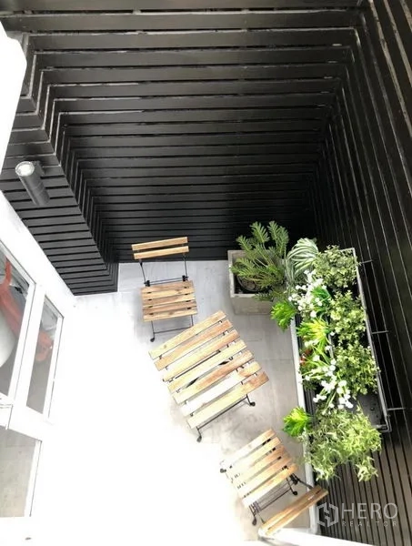 Townhouse for rent in Khlong Toei, Bangkok - Compact patio with wooden bistro set and a vertical garden against black slat walls.