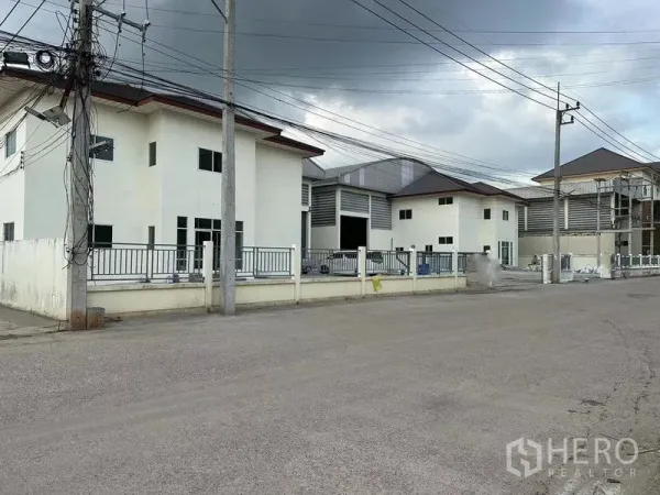 Warehouse for rent in Mueang Samut Sakhon, Samut Sakhon - Gated warehouse compound with office blocks and wide access road in Mueang Samut Sakhon under a cloudy sky.