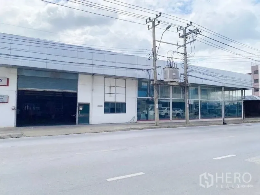 Warehouse for rent in Bang Khen, Bangkok - Wide street frontage of an industrial building with large display windows and a shuttered loading bay.