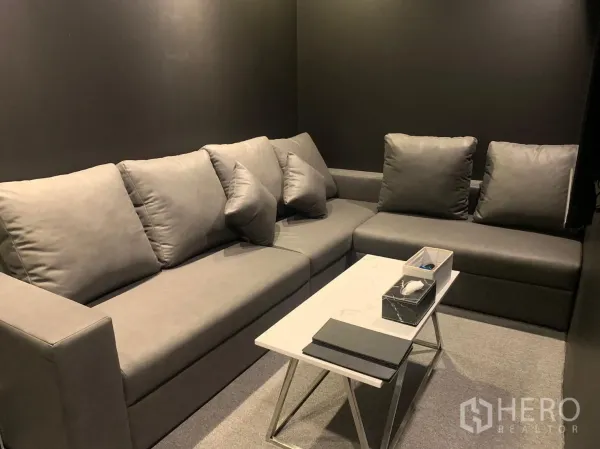 店屋 出租在Bangkok - 小型会客室，灰色沙发与白色茶几，深色墙面。