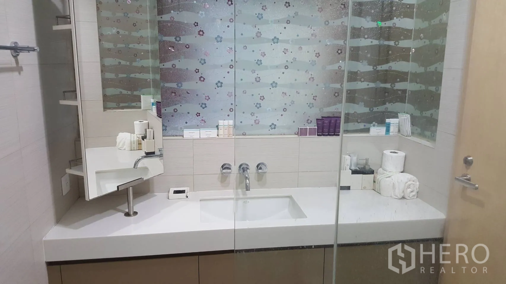 Condominium for rent in Khlong Toei, Bangkok - Wide vanity with mirror, under-counter storage and toiletries in the bathroom.