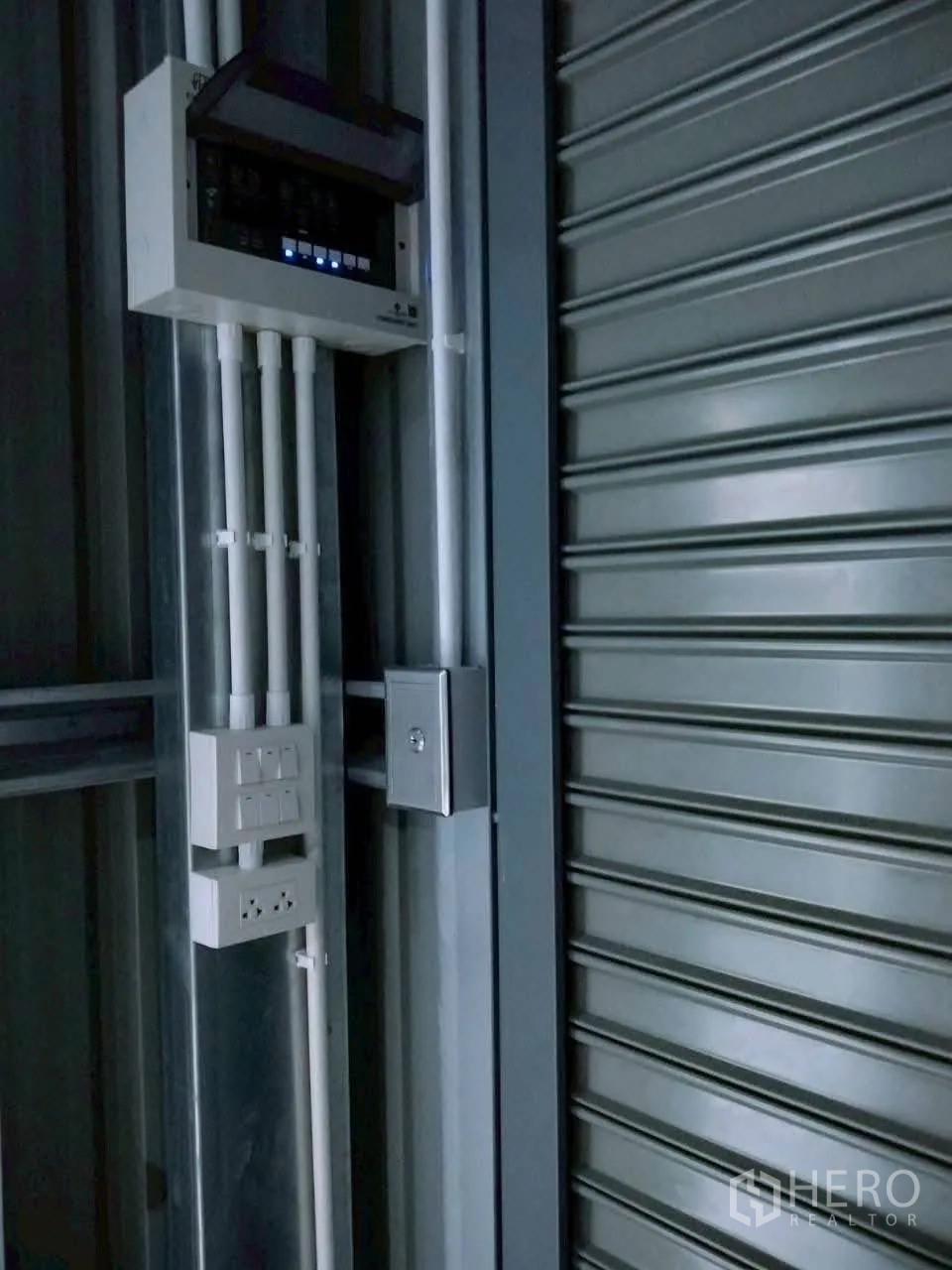 Warehouse for rent in Lat Phrao, Bangkok - Close-up of the electrical panel and outlets next to a metal roller shutter inside the warehouse.