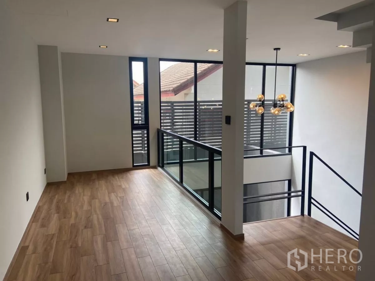 Townhouse for rent in Huai Khwang, Bangkok - Upper lounge with wood floors and floor-to-ceiling windows beside the void.